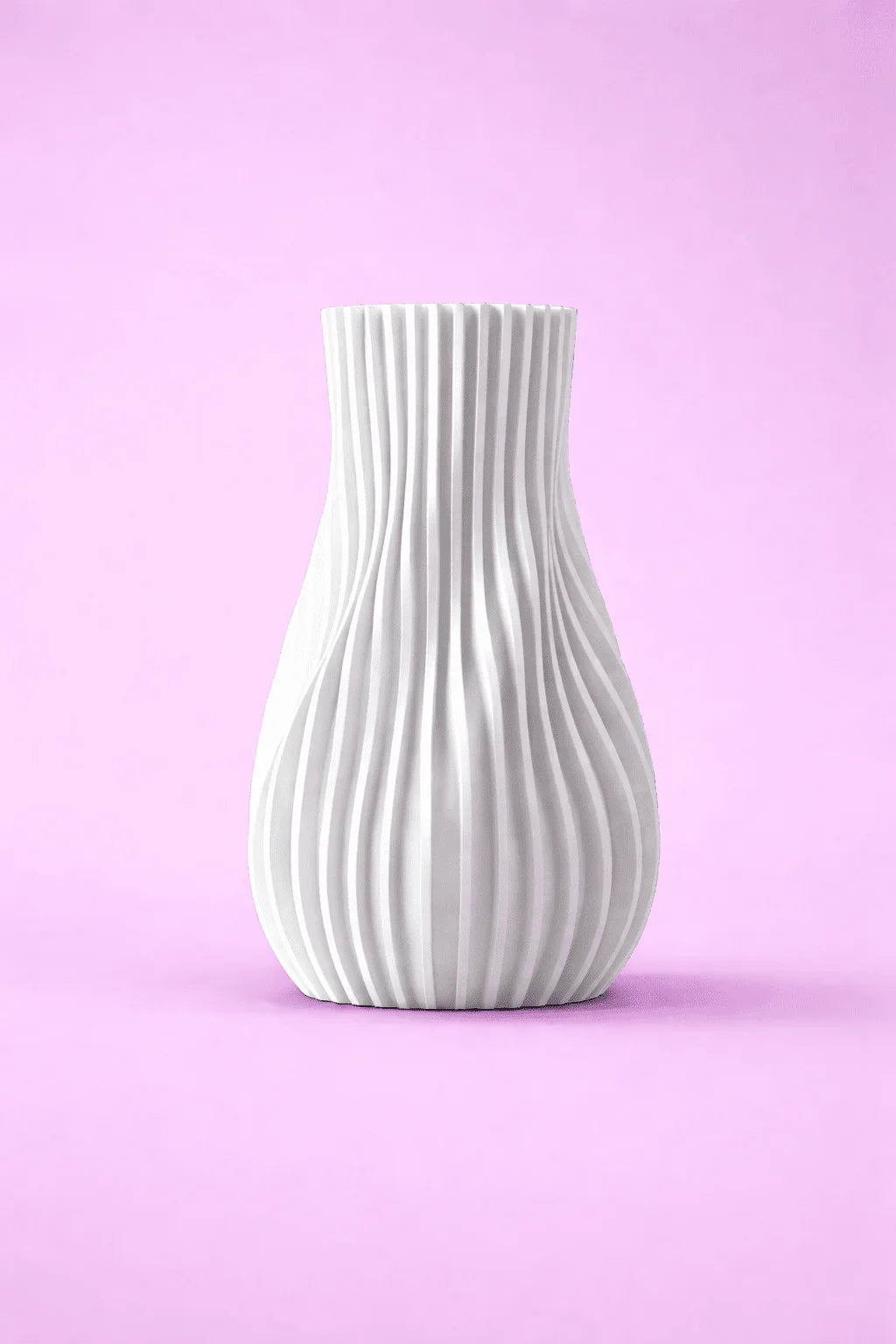 Jarrón blanco moderno impreso en 3D con diseño ondulado sobre fondo rosa.