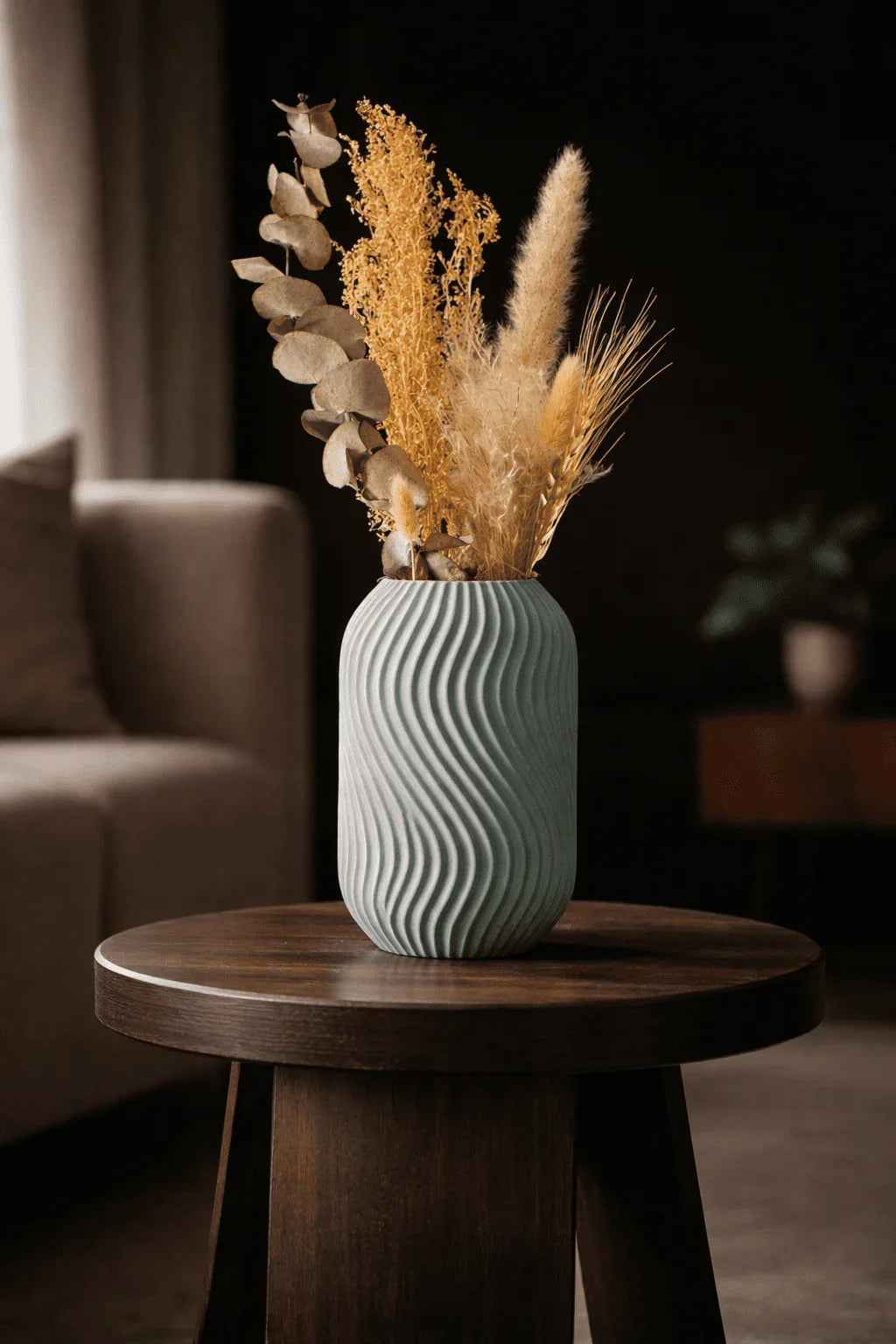 Jarrón decorativo gris con textura ondulada y ramos secos sobre mesa de madera en sala moderna