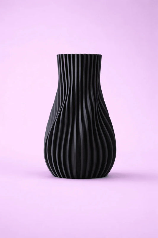 Jarrón negro de diseño moderno con textura ondulada, sobre fondo rosa claro.