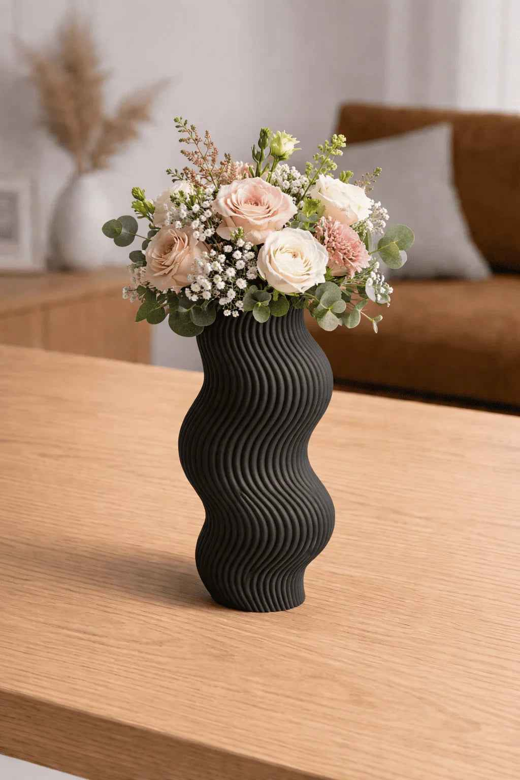 Jarrón negro ondulado con ramo de flores rosas y blancas sobre mesa de madera en sala moderna