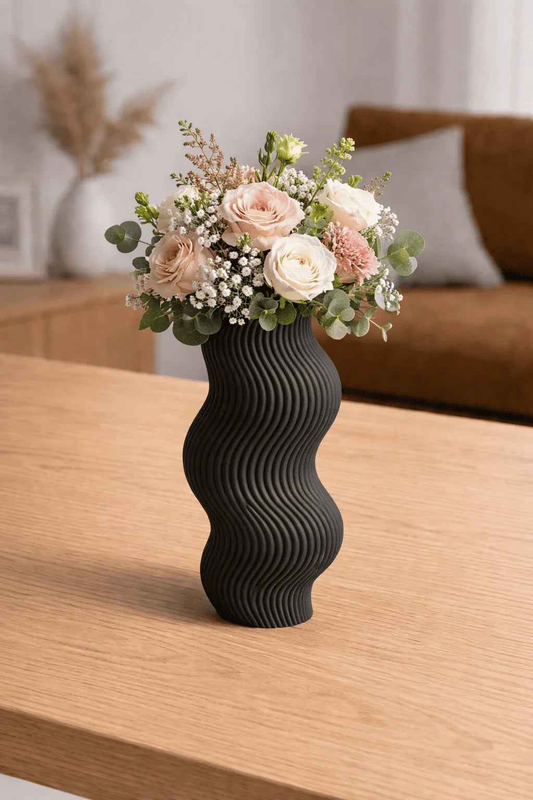 Jarrón negro ondulado con ramo de flores rosas y blancas sobre mesa de madera en sala moderna