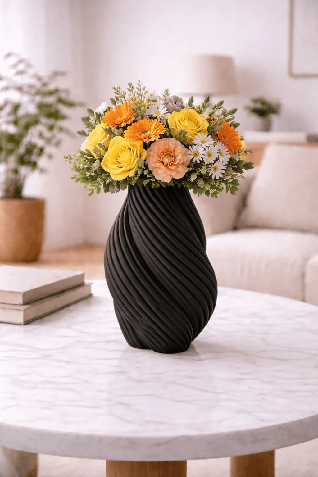 Jarrón negro moderno con flores amarillas, naranjas y blancas sobre mesa de sala elegante