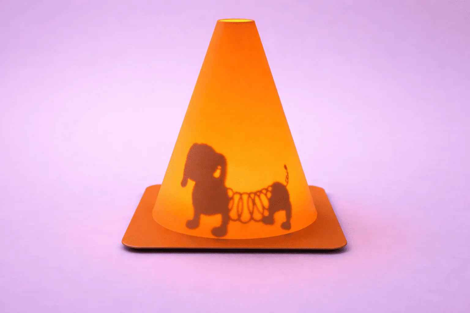 Lámpara decorativa naranja con sombra de perro sobre fondo lila minimalista