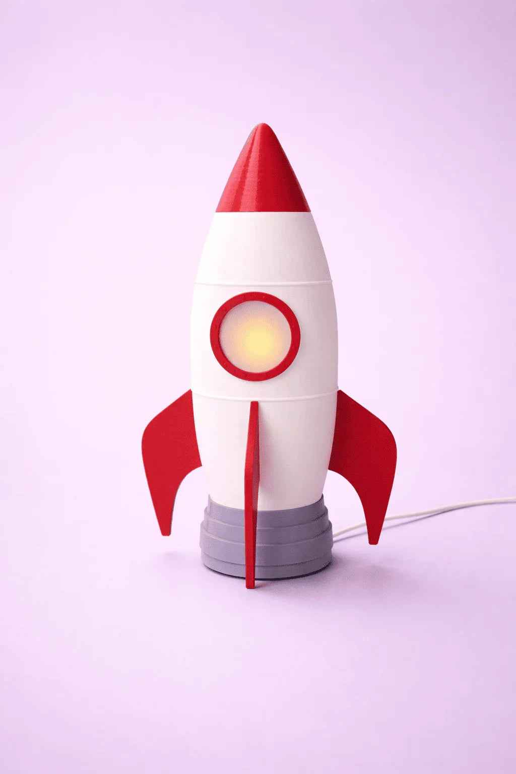 Lámpara cohete blanco y rojo de diseño 3D sobre fondo violeta claro, decoración infantil.