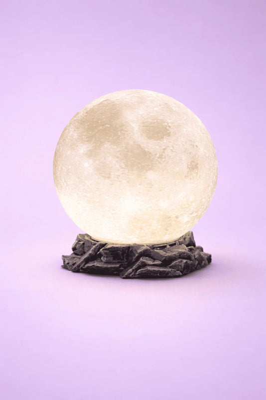 Lámpara luna 3D con base de roca sobre fondo morado, luz decorativa moderna