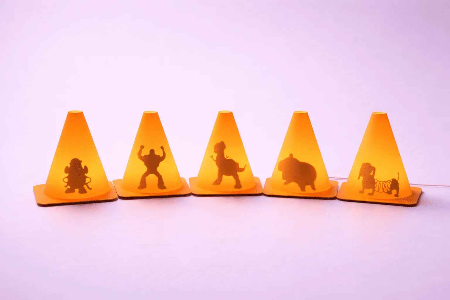 Conos naranjas iluminados con siluetas de personajes y animales, fondo lila