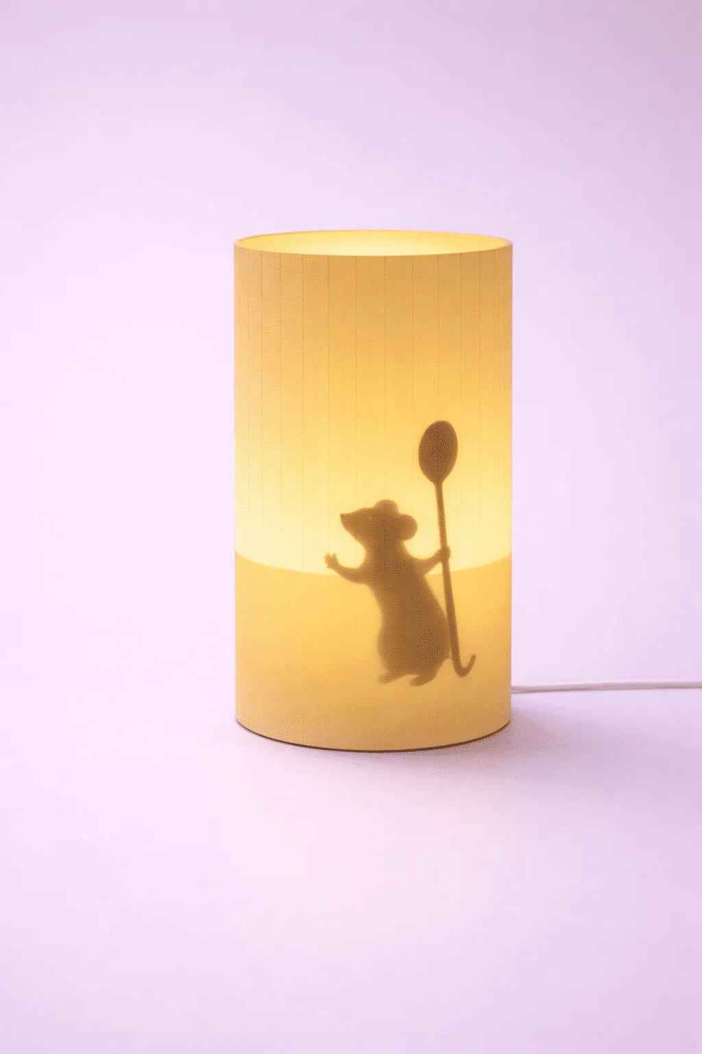 Lámpara decorativa cilíndrica con silueta de ratón sosteniendo cuchara, fondo morado.