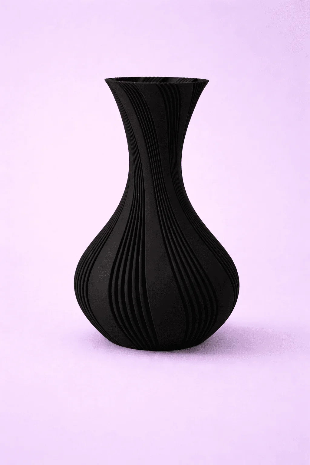 Florero negro impreso en 3D con diseño moderno y líneas onduladas sobre fondo rosa claro