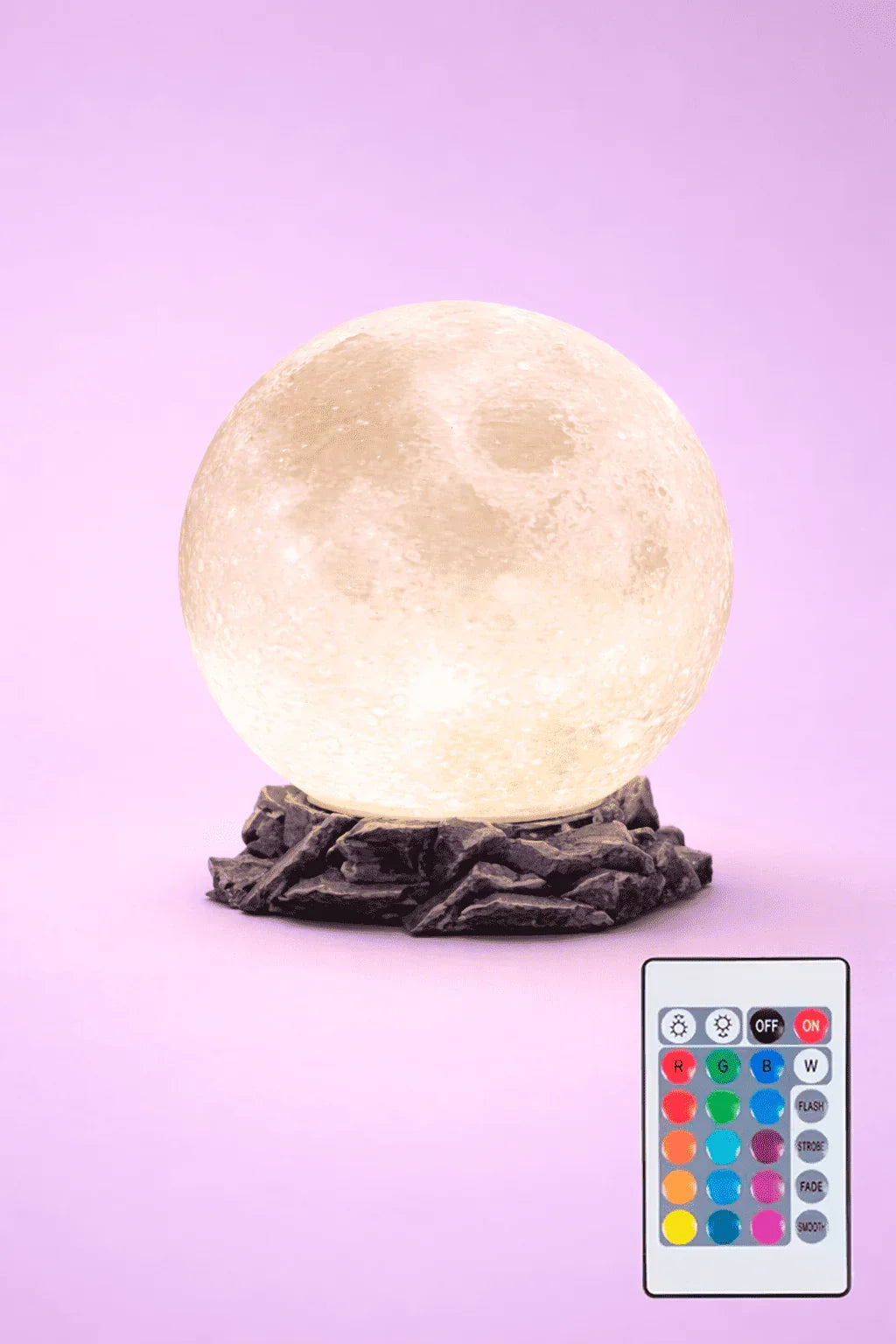 Lámpara lunar 3D con base de roca y control remoto multicolor sobre fondo lila.