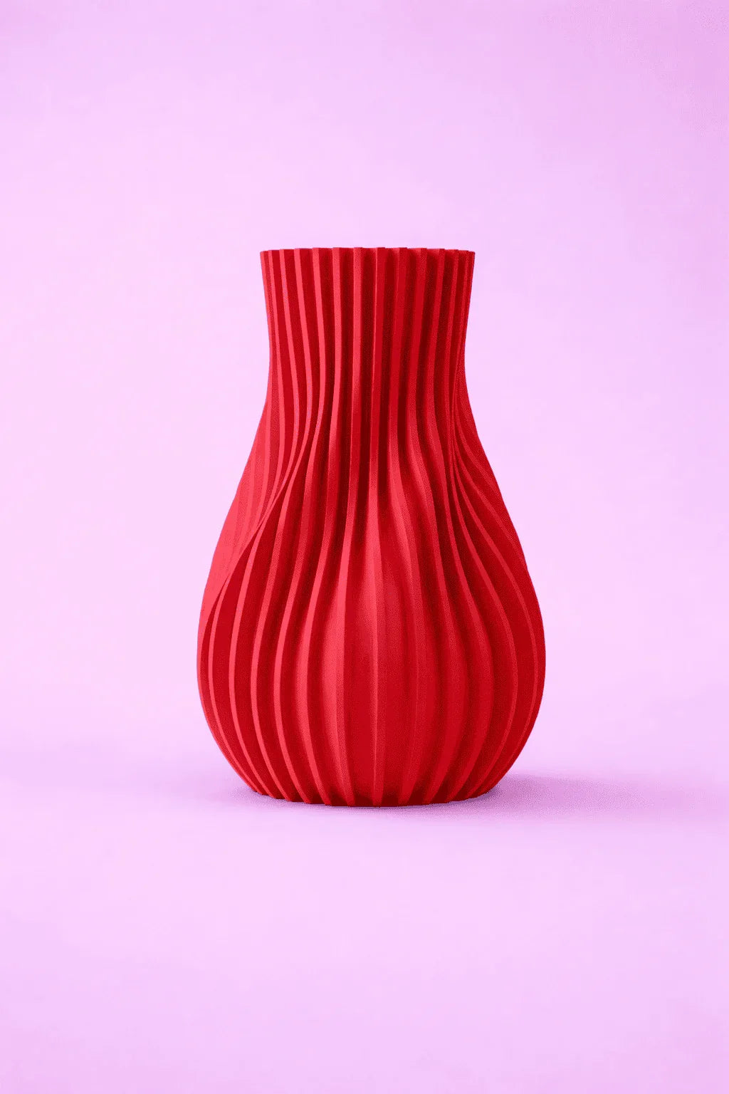 Jarrón rojo impreso en 3D con diseño geométrico sobre fondo rosa
