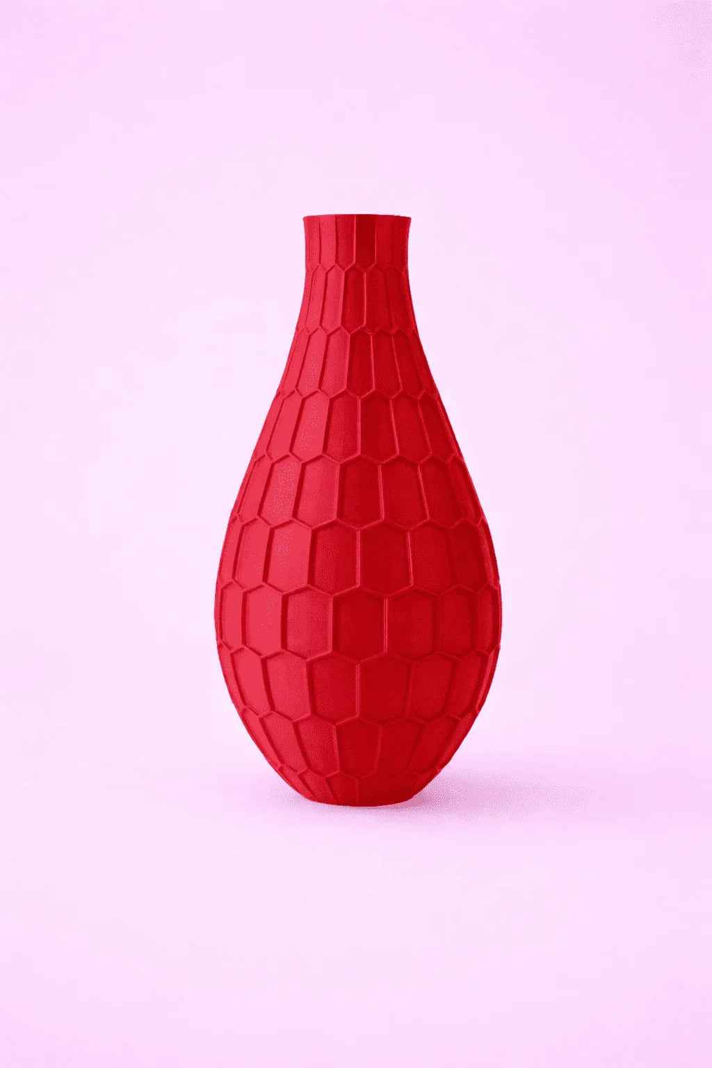 Jarrón rojo impreso en 3D con textura geométrica, fondo rosa claro.