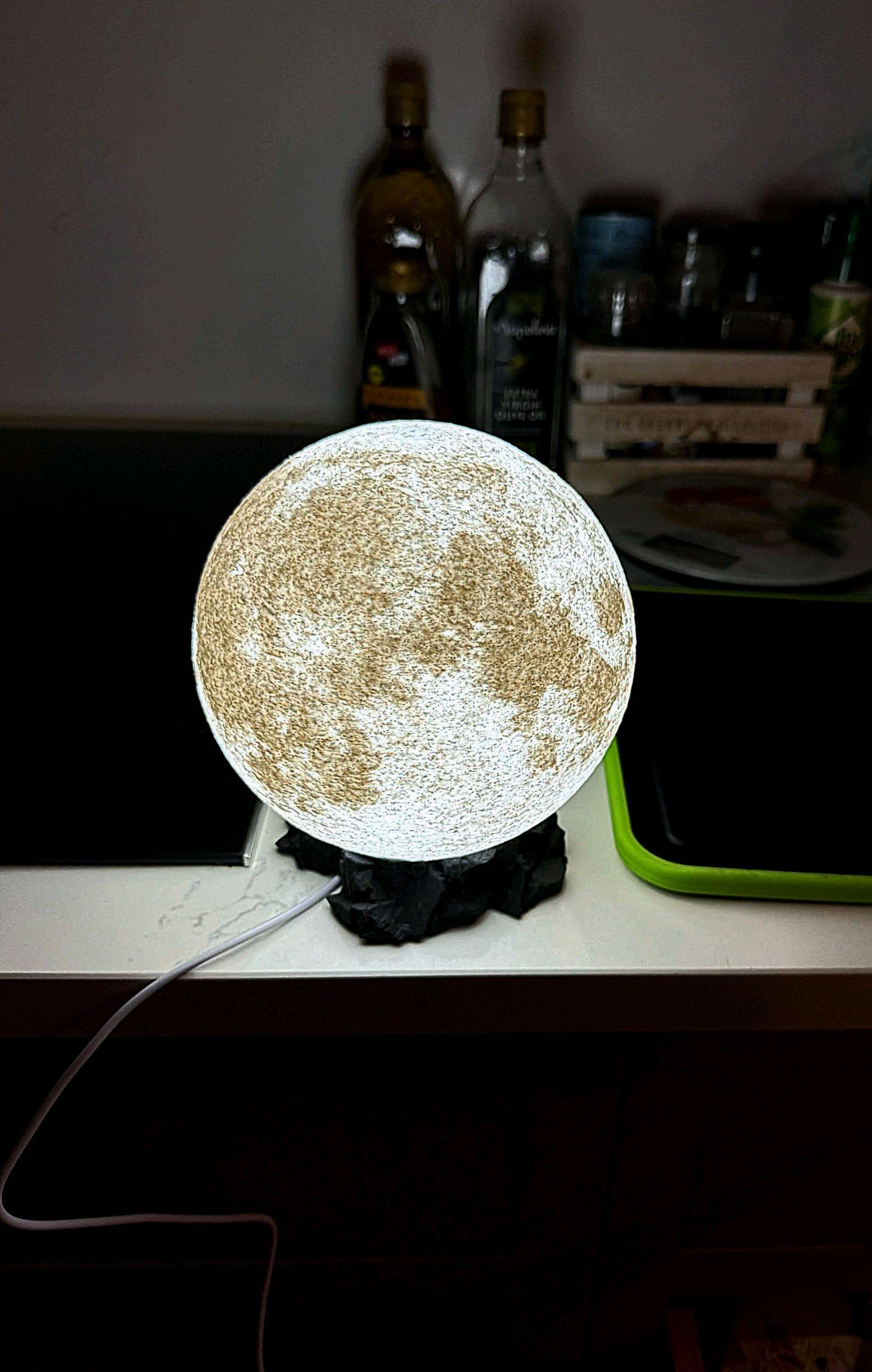 Lámpara nocturna LED con forma de luna encendida sobre mesa de cocina, decoración moderna.
