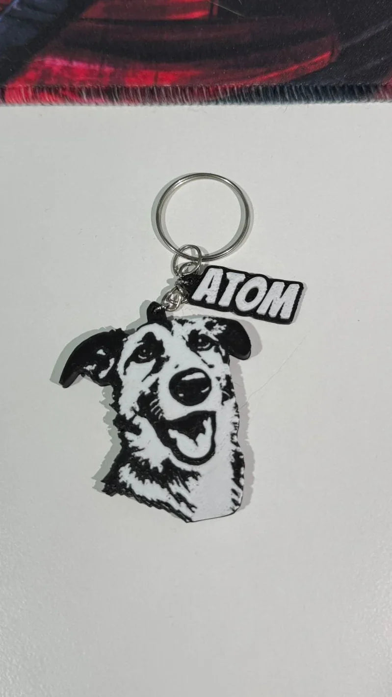 Llavero personalizado de perro en blanco y negro con nombre 'Atom', fondo blanco.